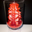 Duża świeca w szklanym kloszu na podsypce z czerwonych kamyczków